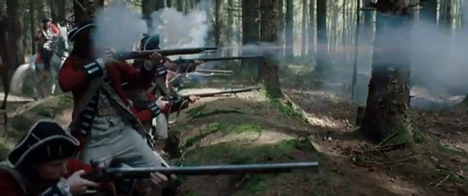 British redcoats in tricorn hats kneel and stand in a pine woods, muskets leveled through white gun smoke